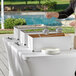 A woman using a Choice disposable chafing dish kit to prepare food on a table outdoors.