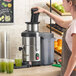 A stainless steel automatic juicer with pulp ejection being used on a kitchen counter.