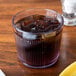 A Carlisle clear plastic tumbler with a drink and ice on a table.