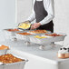 A man in a black apron holding a tray of food over a metal container with a copper bowl inside.