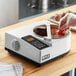 A hand dipping a strawberry into a bowl of chocolate on a ChocoVision chocolate tempering machine.