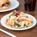 A white Dart foam plate with pasta and a sandwich on it.