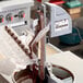 A person using a ChocoVision skimmer to pour chocolate into a machine.