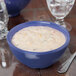 A peacock blue melamine bowl filled with white liquid soup on a table.