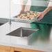 A person holding a tray of food with shrimp and rice over a metal drop-in hot food well.