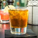 A Libbey double old fashioned glass filled with ice and brown liquid with a lemon slice on top.