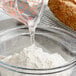 A measuring cup pouring clear liquid into a bowl of white powder.