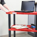 A woman using a red Luxor Tuffy utility cart with a laptop on it.