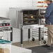 A man standing next to a MainStreet Equipment convection oven with bread on a tray.