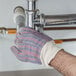 A hand wearing Cordova leather work gloves fixing a pipe.