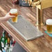 A rectangular stainless steel surface mount beer drip tray with circular holes, placed on a wooden bar counter next to a beer tap.