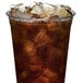 A plastic cup with ice and brown liquid in it sitting on a table with a white background.