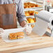 A person in a brown apron holding a sandwich wrapped in Choice 40 lb. wet wax paper.