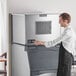 A man in an apron standing next to a Scotsman air cooled medium cube ice machine.