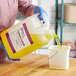 A woman in blue gloves pouring yellow Lemon Lance liquid into a white bucket.