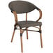 A Lancaster Table & Seating round wooden table with two brown wicker arm chairs with black cushions.