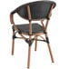 A close up of a Lancaster Table & Seating black wicker arm chair with a wooden frame and black seat.