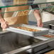 A full size stainless steel food pan filled with cooked food being placed into a buffet or cafeteria serving station.