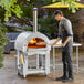 A man cooking pizza in a Backyard Pro wood-fired oven on a table.