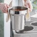 A person holding a pot of hot soup in a silver chafer food pan.