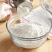 A person using a whisk to mix Arrowhead Mills unbleached organic all-purpose flour into a bowl.