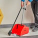 A man using a broom and a Lavex large debris dust pan to sweep a floor.