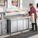 An Avantco stone top pizza prep table with refrigerated topping rail and sneeze guard full of pizza ingredients.