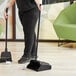 A woman using a Lavex open-lid dustpan to clean up with a broom in a corporate office cafeteria.