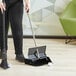 A woman using a Lavex steel dust pan to sweep the floor.