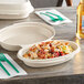 A World Centric fiber burrito bowl container filled with food on a table with a green fork.