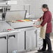 An Avantco countertop refrigerated prep rail with food in containers being prepared by a man in a chef's uniform.