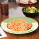 A bowl of spaghetti and salad on a table with an avocado melamine bowl filled with salad.
