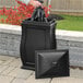 A woman using a Mayne Mansfield black multi-purpose storage bin as a trash can on an outdoor patio.