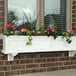 A white planter box with flowers on a brick wall.