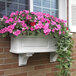 A white planter box with pink flowers on a brick wall.
