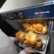 A chef holding a tray of cooked chicken in an Alto-Shaam stackable oven.