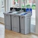 A Rubbermaid landfill recycling station with three grey bins with white lids and different colored labels.