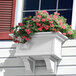 A white Mayne Yorkshire planter with pink flowers on a white wall.