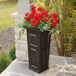 A Mayne espresso planter with red flowers on an outdoor patio table.