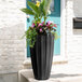 A black Mayne Sedona planter with flowers in it.