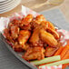 A plate of chicken wings with carrot sticks and a cup of hot honey sauce.