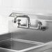 A wall-mounted faucet with 8-inch centers and a 6-inch swing spout installed above a stainless steel sink.