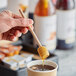 A person holding a Choice wood honey dipper over a cup of honey.