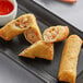 A white plate with The Gourmet Egg Roll Co. shrimp egg rolls and a bowl of red sauce.