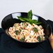 A black slanted melamine bowl with pasta, broccoli, and basil.