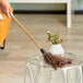 A hand holding a Lavex feather duster with a wooden handle over a glass table.