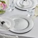 A white table setting with silver Choice charger plates on a white table.