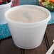 A Dart translucent plastic lid on a white container of soup with a green leaf in it.