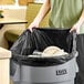 A man holding a black Lavex janitorial can liner over a trash can full of plates.