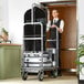 A man in a suit and tie pushing a Lancaster Table & Seating stainless steel bellman cart.